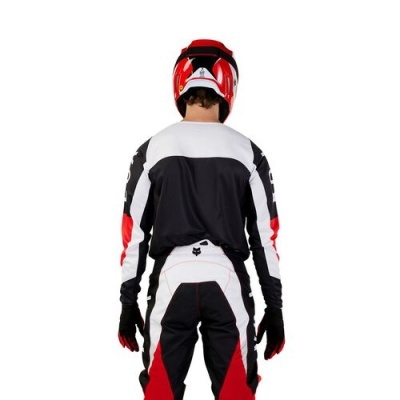 Pessoa com equipamento de motocross visto de costas, incluindo capacete vermelho e roupa preta, branca e vermelha.