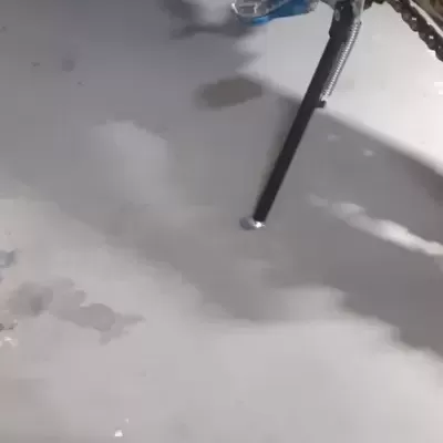 Motocicleta verde com pedal azul e suporte lateral preto sobre chão cinzento