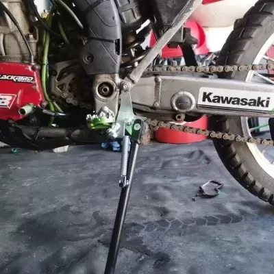 Parte lateral de uma moto Kawasaki com corrente e pé de apoio