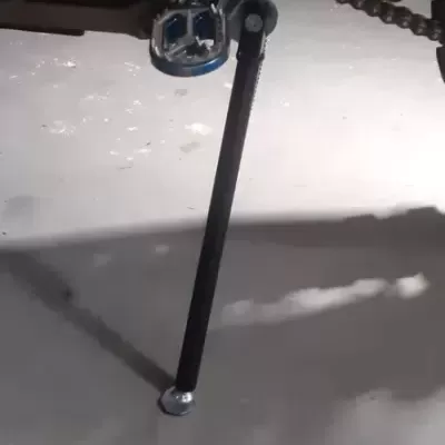 Descanso lateral preto para suporte de motocicleta, fixado ao quadro verde próximo à corrente.