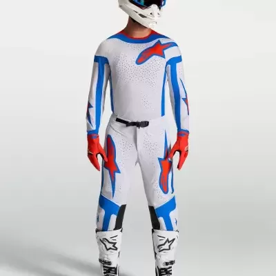 Equipamento motocross branco com detalhes azuis e vermelhos e capacete com óculos azuis