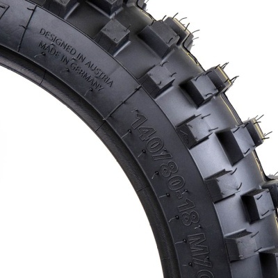 Pneu preto grosso com cravos e números visíveis em fundo branco