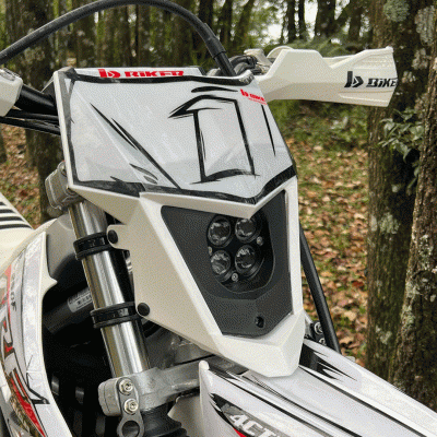 Motocross branco com farol de LED e adesivos em ambiente florestal