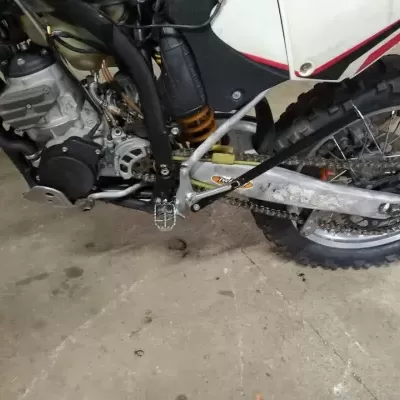 Motocross branca, vermelha e preta com pneus de cravos e motor visível