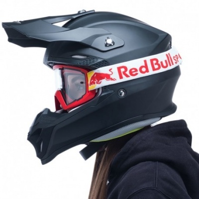 Capacete de motocross preto com viseira e óculos vermelhos com correia Red Bull, usado por pessoa com capuz preto.