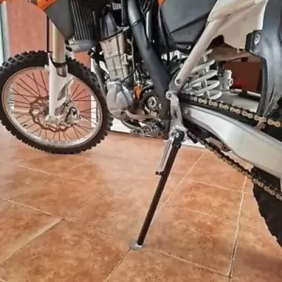Motocross laranja e preto com suporte abaixado em chão de azulejo castanho claro