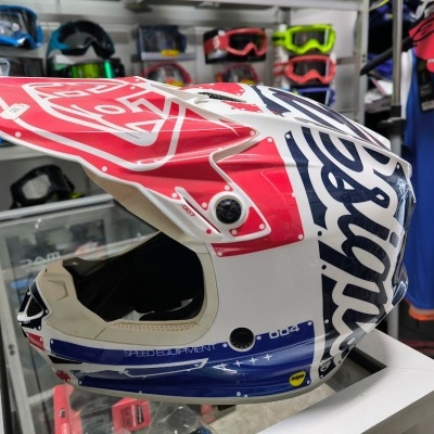 Capacete motocross branco, vermelho e azul com padrões gráficos, loja ao fundo