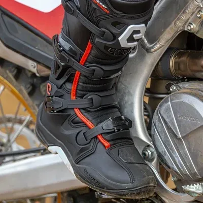Bota preta de motocross com detalhes vermelhos numa mota Honda
