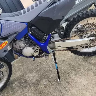 Motociclo Yamaha azul e cinzento com pneus fora de estrada e autocolantes UFO e FMF.