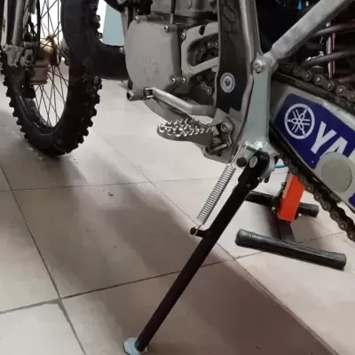 Mota de motocross Yamaha com suporte lateral e corrente numa superfície de azulejo.