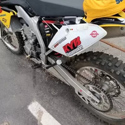 Moto de cross Suzuki amarela, preta e branca com textos KYB Suspension, MOTORPORTUGAL e outros em pavimento de asfalto