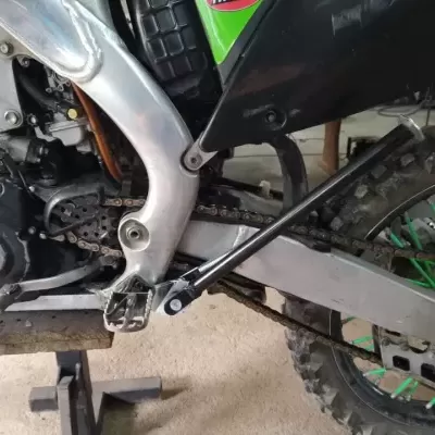 Motocicleta de motocross com motor e quadro metálico prateado e roda traseira com pneus grossos e raios verdes