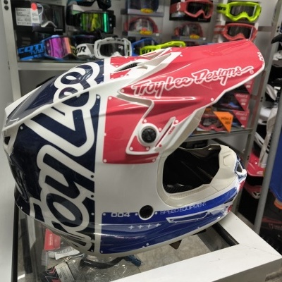 Capacete integral motocross Troy Lee Designs branco, azul e vermelho exibido em loja.