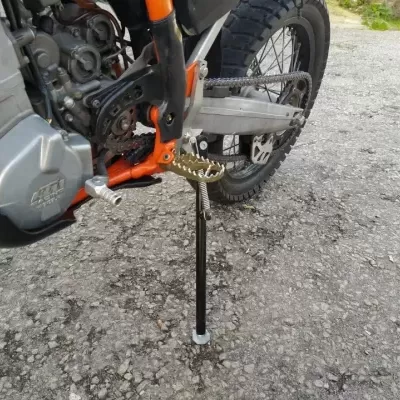 Mota laranja com motor metálico e descanso lateral preto em asfalto