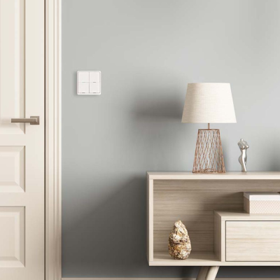 Interruptor branco de quatro botões numa parede cinza ao lado de porta branca e consola de madeira clara com abajur e decoração