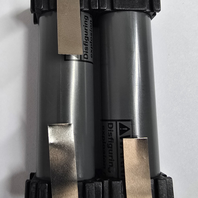 Dois cilindros cinzentos com pontas pretas e tiras metálicas, texto 'Disfiguring' visível.