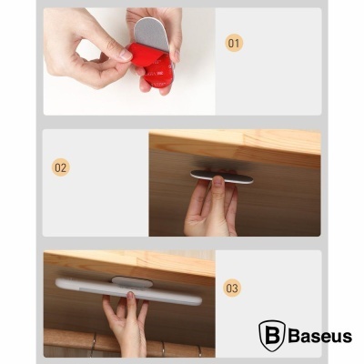 Acessório Baseus cinzento com adesivo vermelho sendo fixado em móvel de madeira