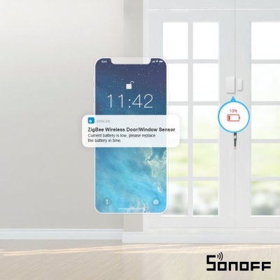 Sensor sem fios ZigBee para porta/janela branco em porta de vidro branca com telemóvel indicando bateria fraca
