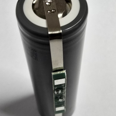 Bateria cilíndrica preta com painel metálico e componentes eletrónicos verdes