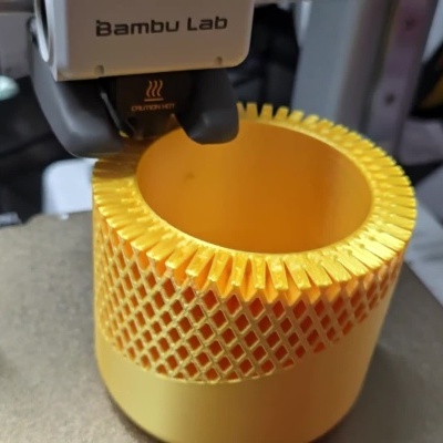 Impressora 3D Bambu Lab a imprimir objeto cilíndrico amarelo com padrão em malha.
