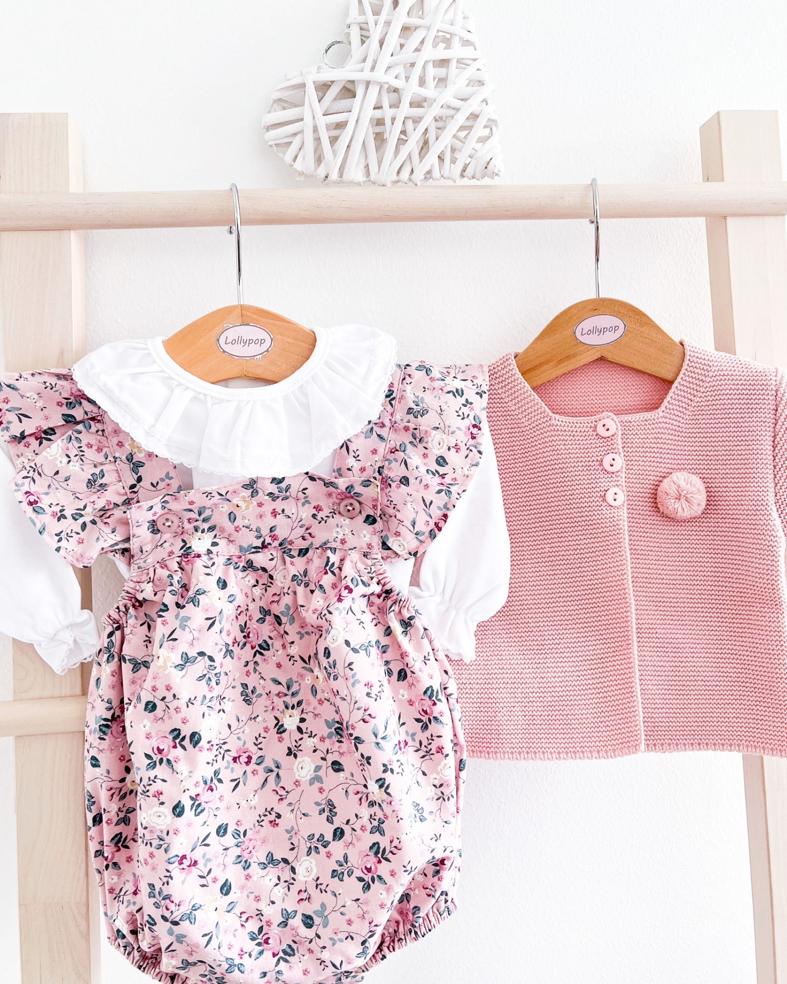 Conjunto de bebé com vestido floral rosa e casaco rosa pendurados em cabides de madeira