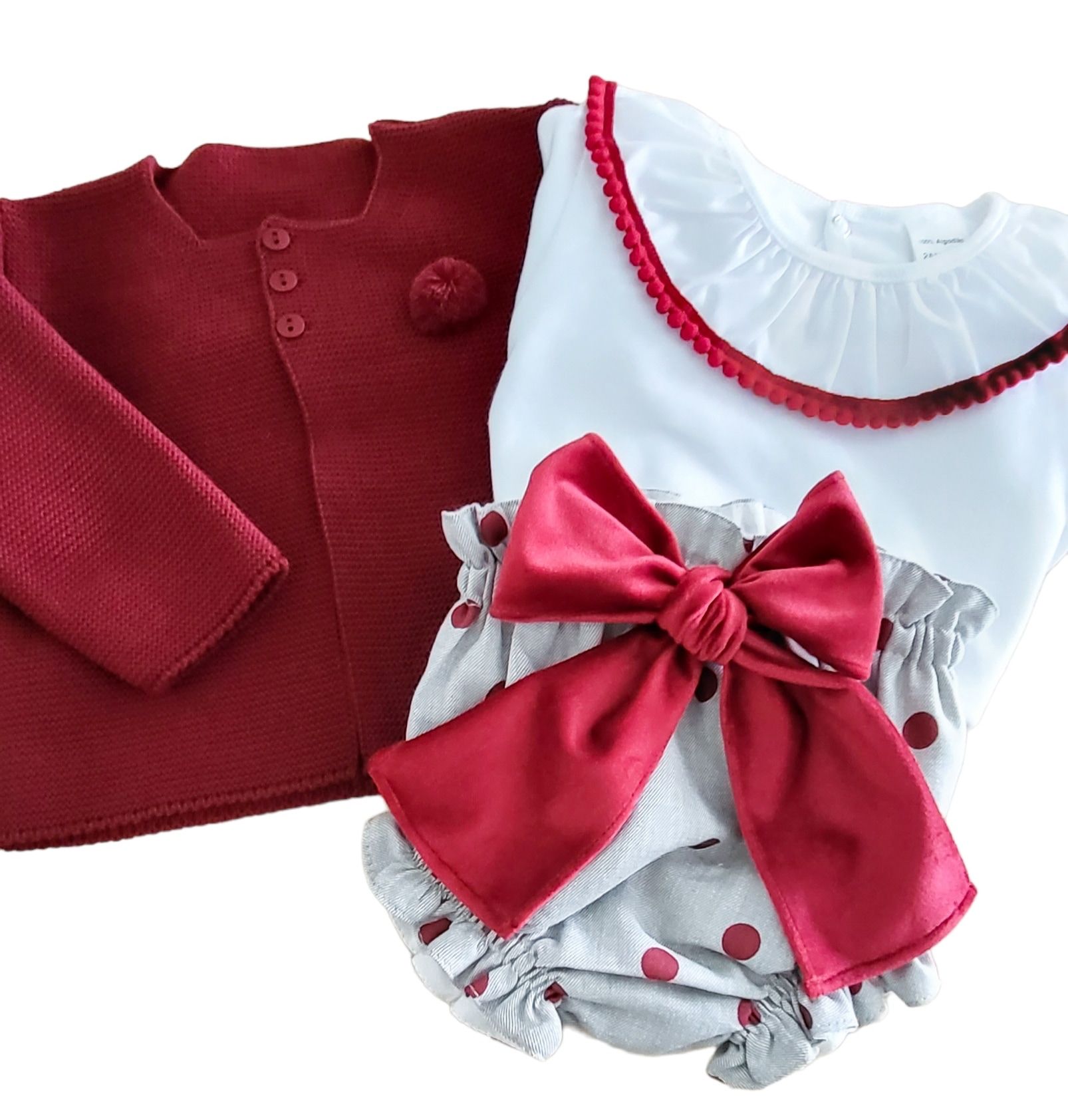 Conjunto de roupa infantil com casaco vermelho, camisola branca e calções cinza com laço vermelho