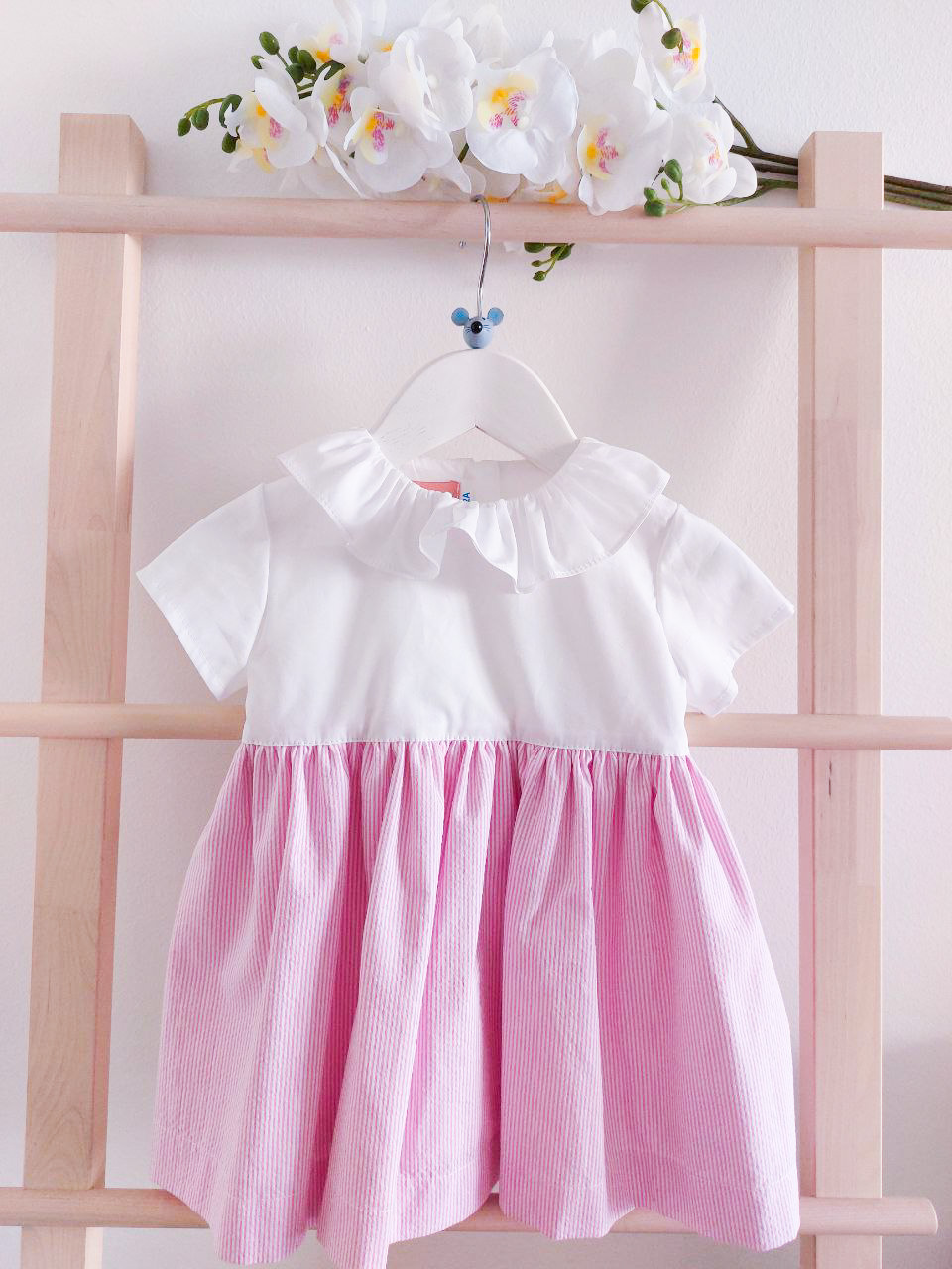 Vestido infantil branco e rosa pendurado com flores brancas no topo