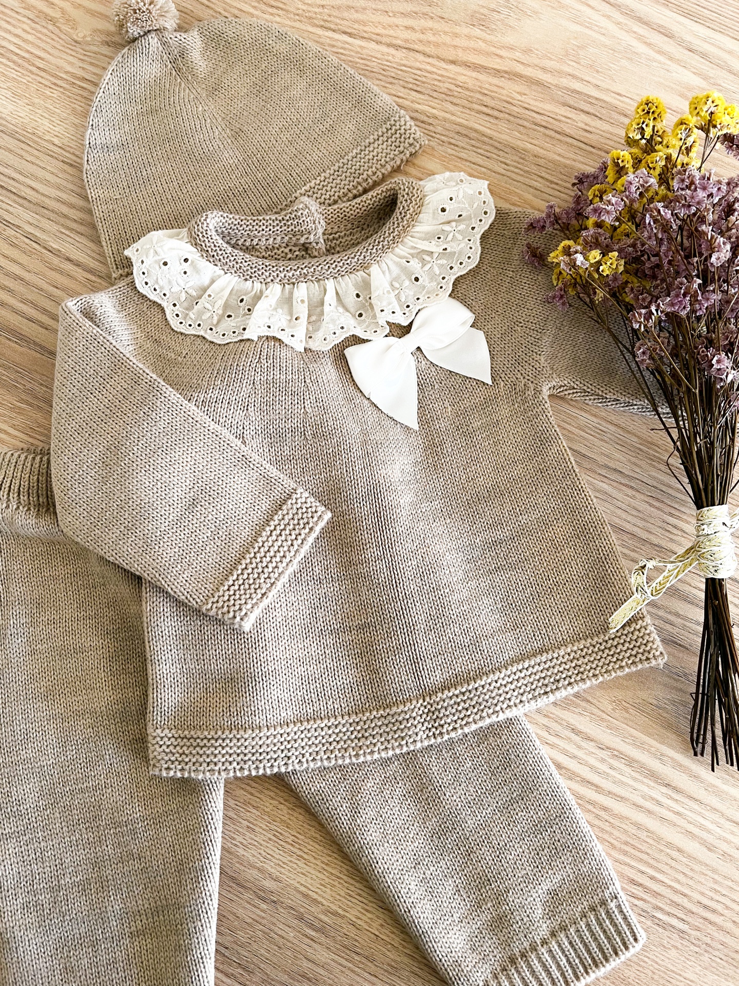 Conjunto de bebé em malha bege com folho branco e laço, calças e gorro com pompom