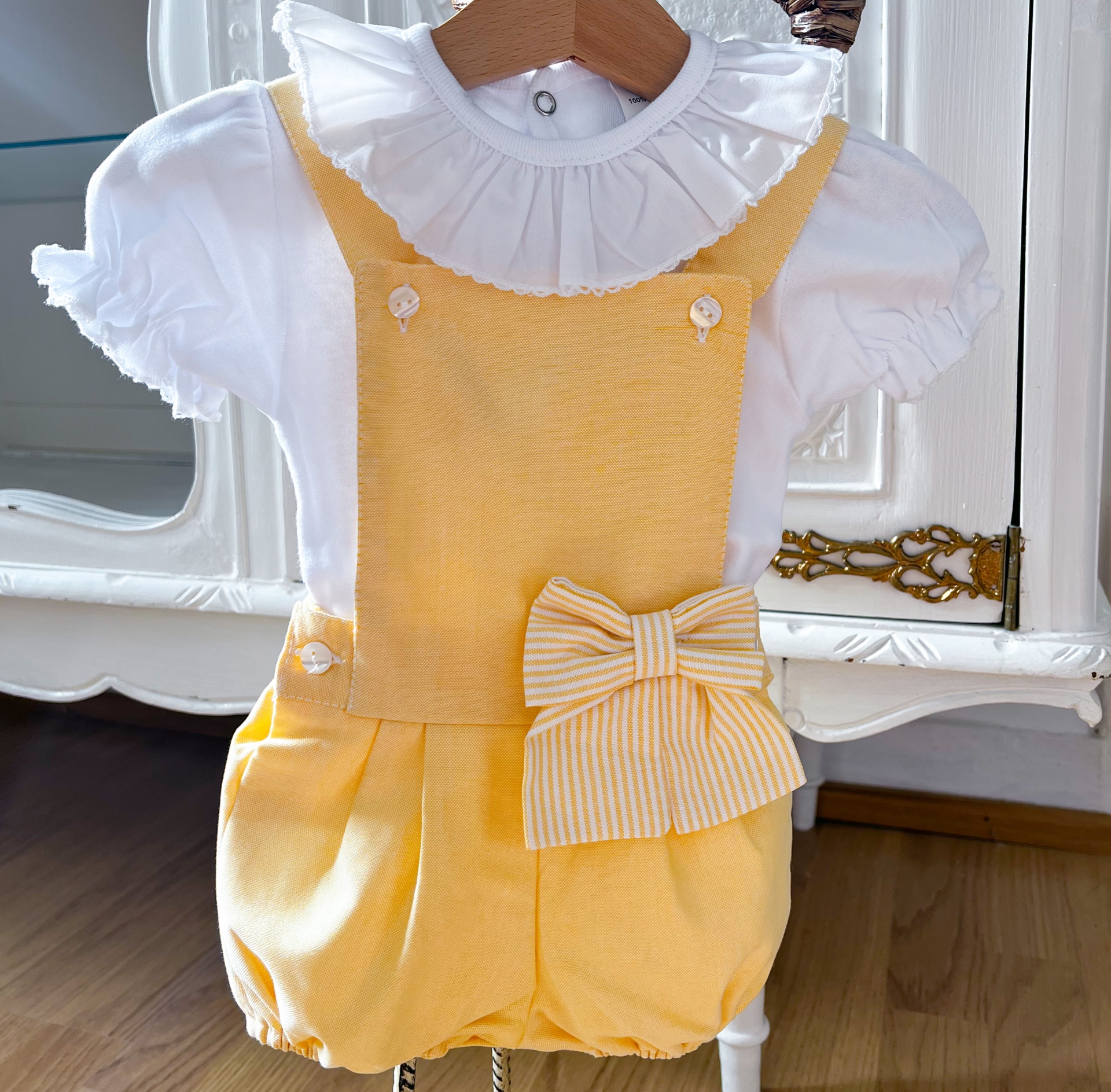 Conjunto infantil branco e amarelo com calção e body exibido num cabide de madeira.