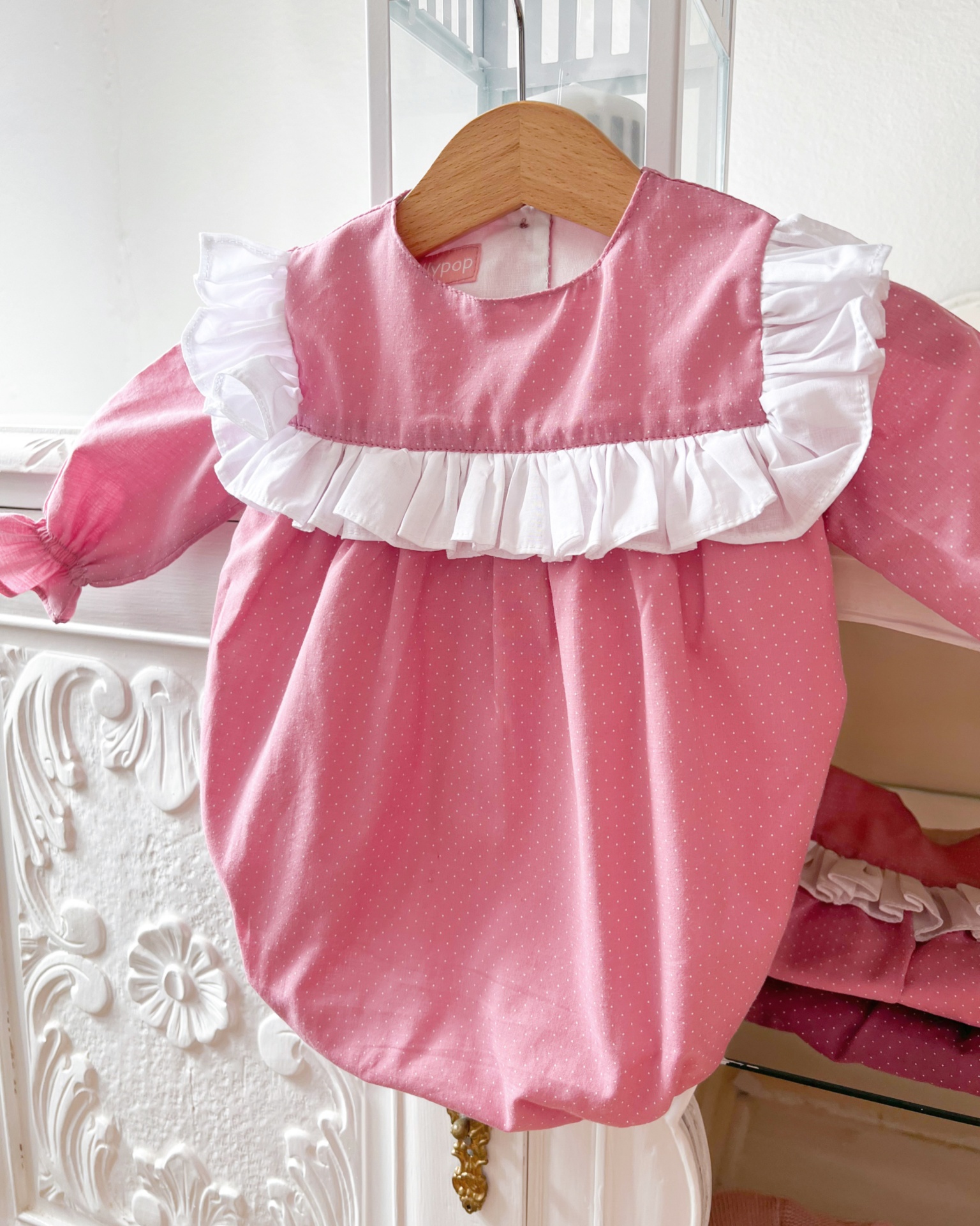 Babygrow rosa com folhos brancos pendurado numa cabide de madeira