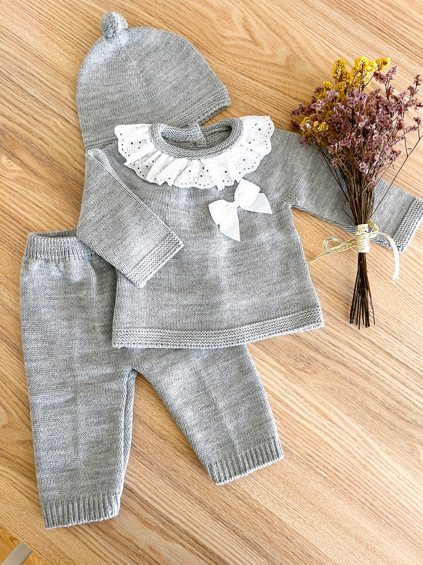 Conjunto de roupa de bebé cinzenta em malha com gola branca rendada e laço, com gorro e flores secas
