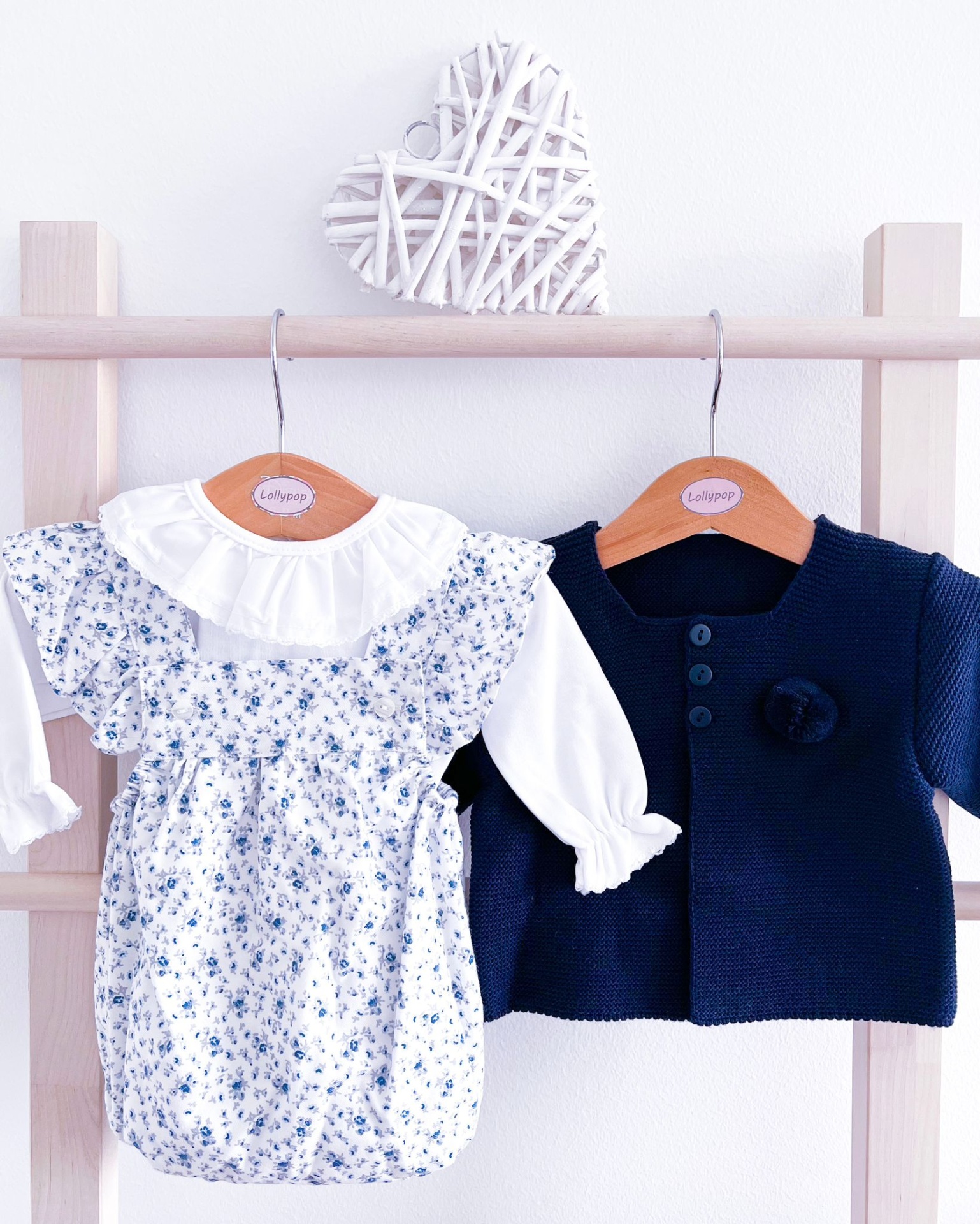 Conjunto infantil com body branco floral azul e casaco azul-marinho pendurados em cabides de madeira