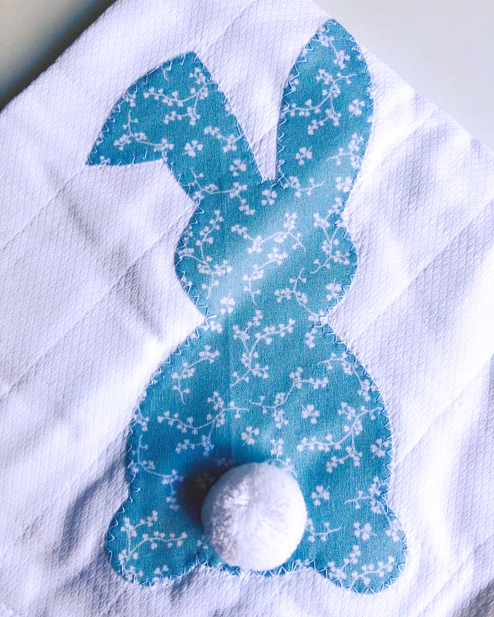 Pano branco com coelho azul floral aplicado e rabo de bola branca