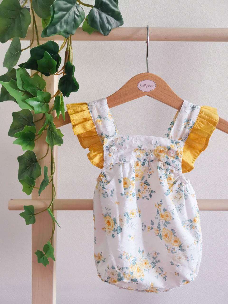 Body de bebé com padrão floral e mangas amarelas pendurado em cabide de madeira