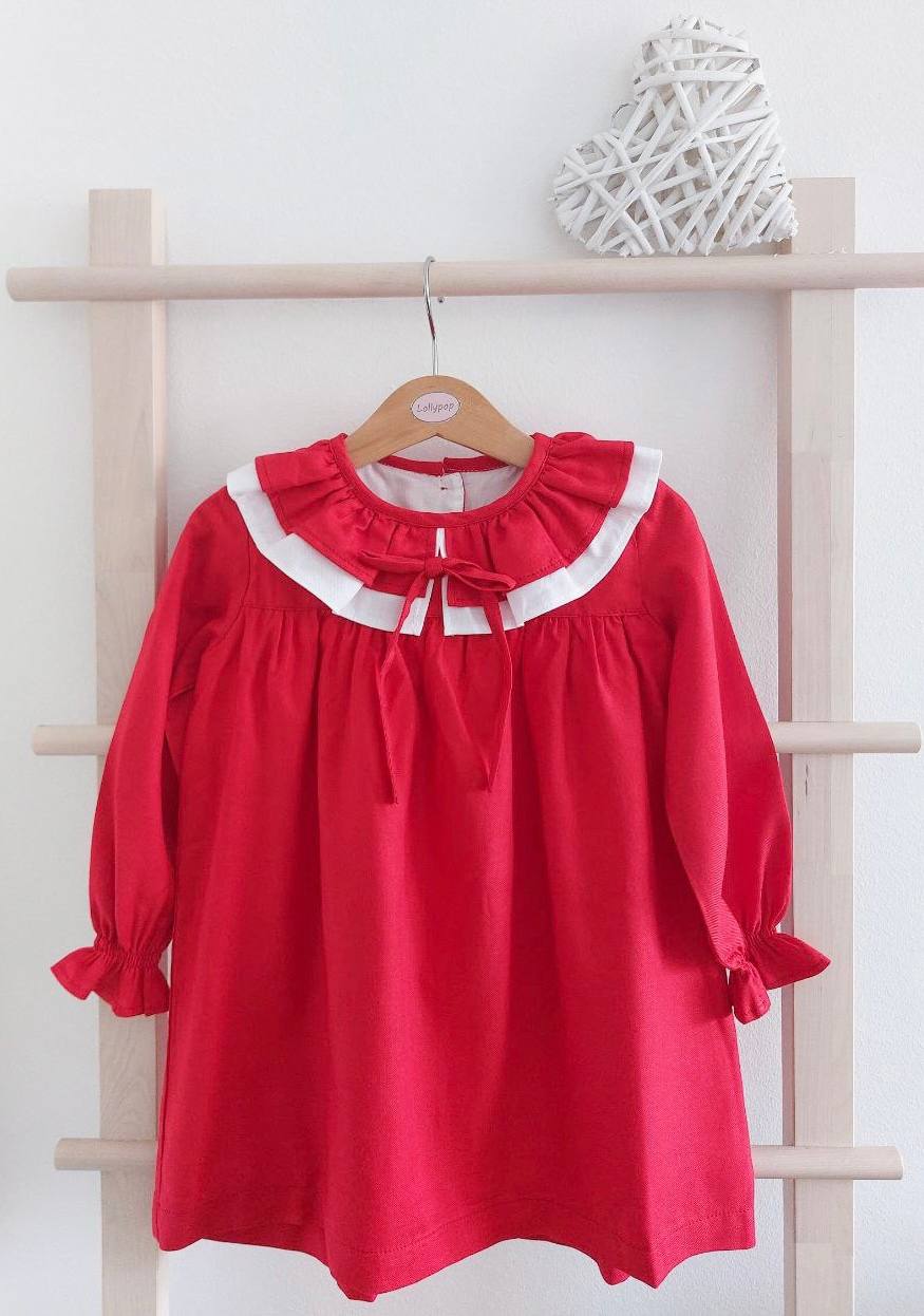 Vestido infantil vermelho com gola branca e laço vermelho pendurado em cabide de madeira