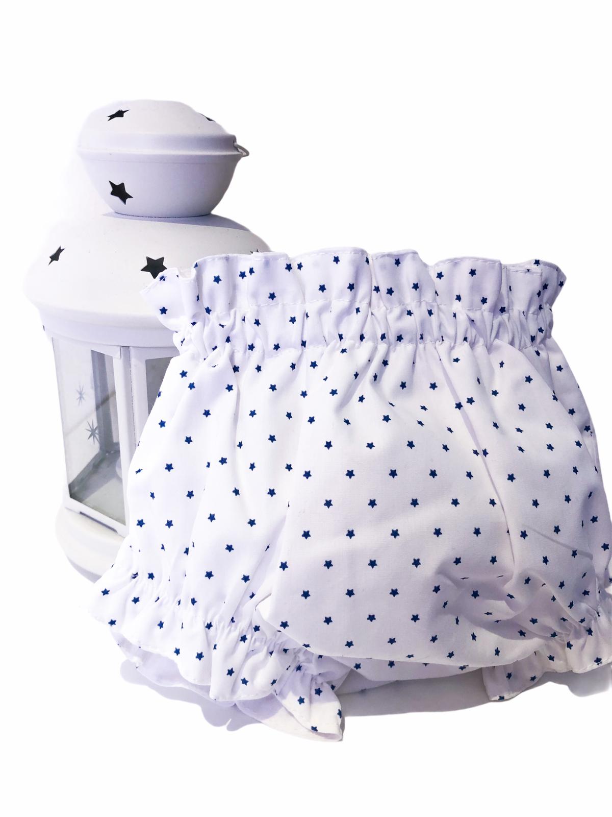 Cueca de bebé branca com estrelas azuis ao lado de um candeeiro branco com estrelas
