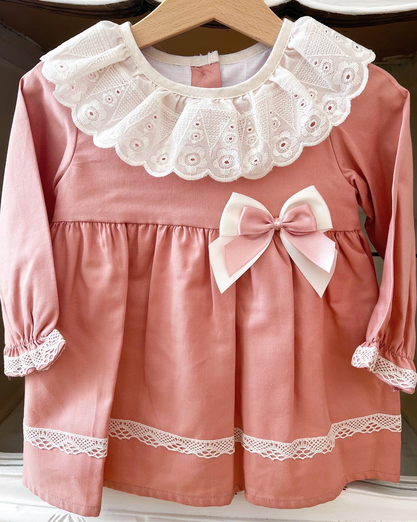 Vestido infantil rosa com gola branca bordada, laço rosa e creme, e detalhes de renda