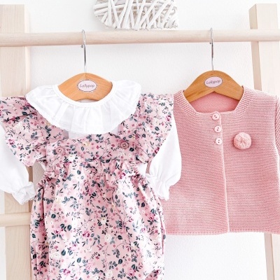 Conjunto de bebé com vestido floral rosa e casaco rosa pendurados em cabides de madeira