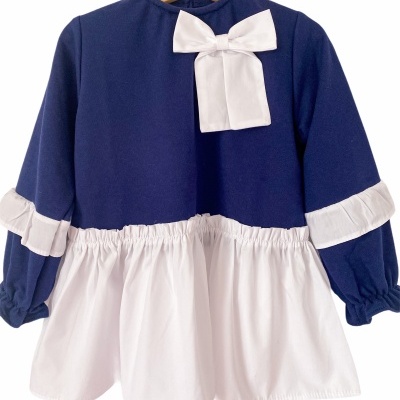 Vestido infantil azul escuro com saia branca e laço branco pendurado em cabide de madeira