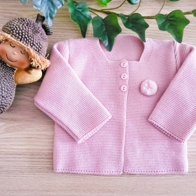 Casaco de malha rosa claro para bebé com botões, sobre mesa de madeira clara