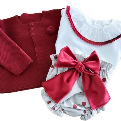 Conjunto de roupa infantil com casaco vermelho, camisola branca e calções cinza com laço vermelho