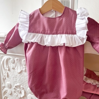 Body rosa com bolinhas brancas e folhos brancos pendurado em cabide de madeira