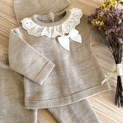 Conjunto de bebé em malha bege com folho branco e laço, calças e gorro com pompom