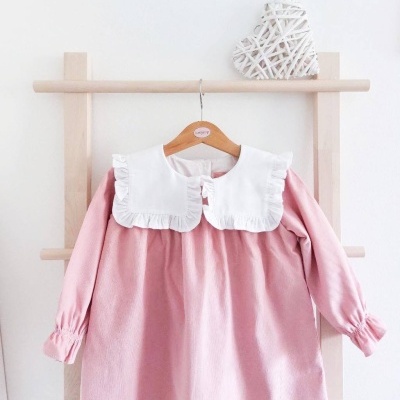 Vestido infantil rosa com gola branca grande e folhos pendurado num cabide de madeira