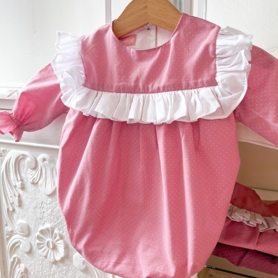 Babygrow rosa com folhos brancos pendurado numa cabide de madeira