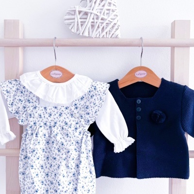 Conjunto infantil com body branco floral azul e casaco azul-marinho pendurados em cabides de madeira