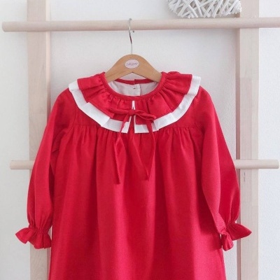 Vestido infantil vermelho com gola branca e laço vermelho pendurado em cabide de madeira