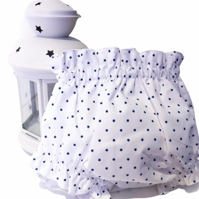 Cueca de bebé branca com estrelas azuis ao lado de um candeeiro branco com estrelas