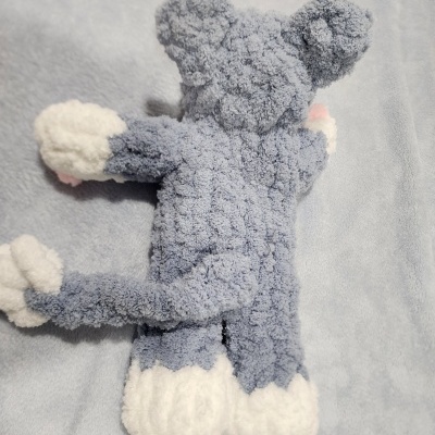 Boneco de peluche cinzento e branco com textura felpuda sobre tecido azul claro