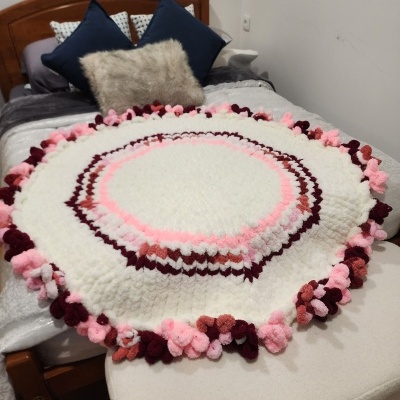 Tapete redondo tricotado com pompons em tons de rosa e vermelho